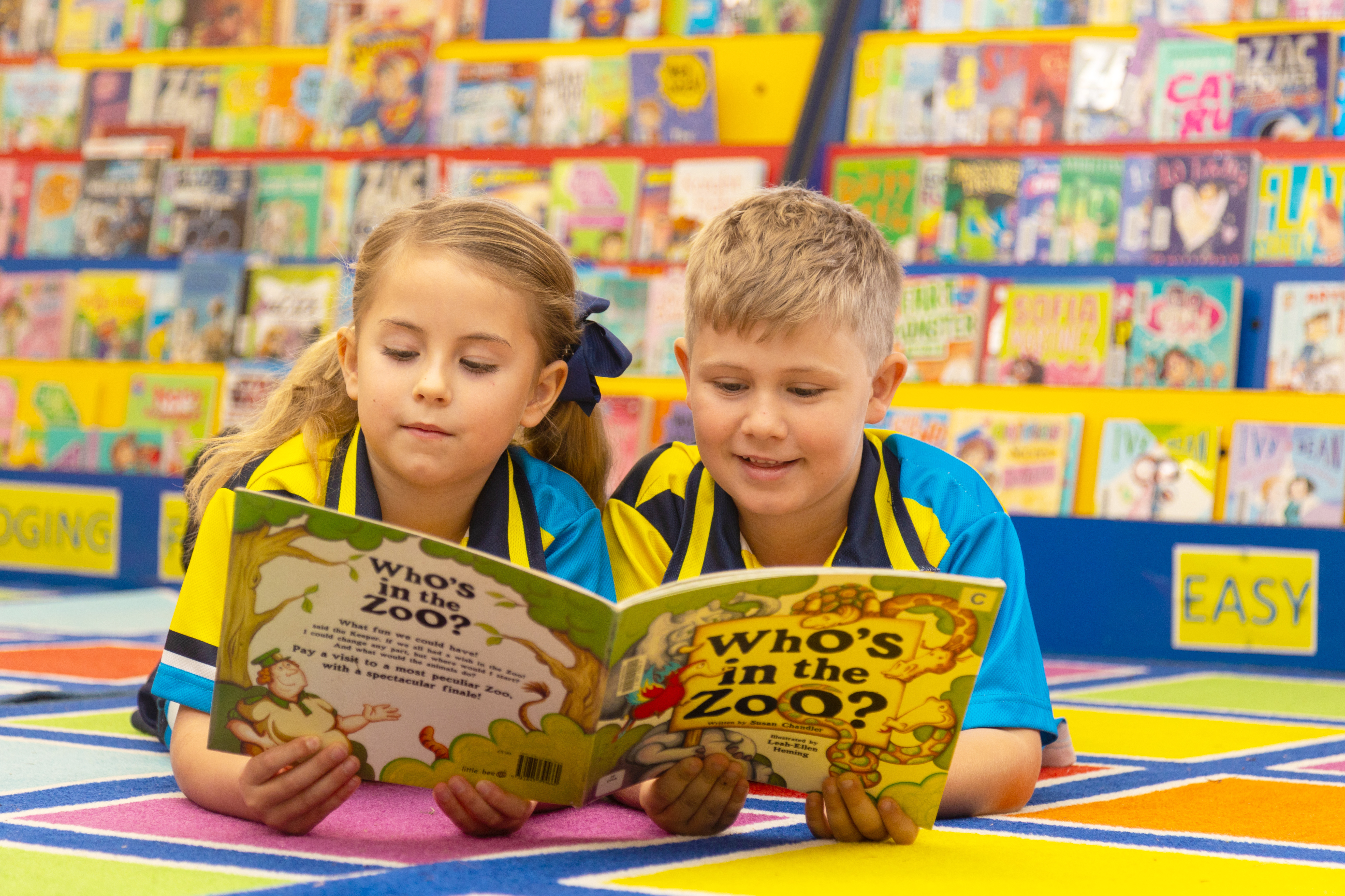 Students in school uniforms lying on the floor reading a book together in a library area